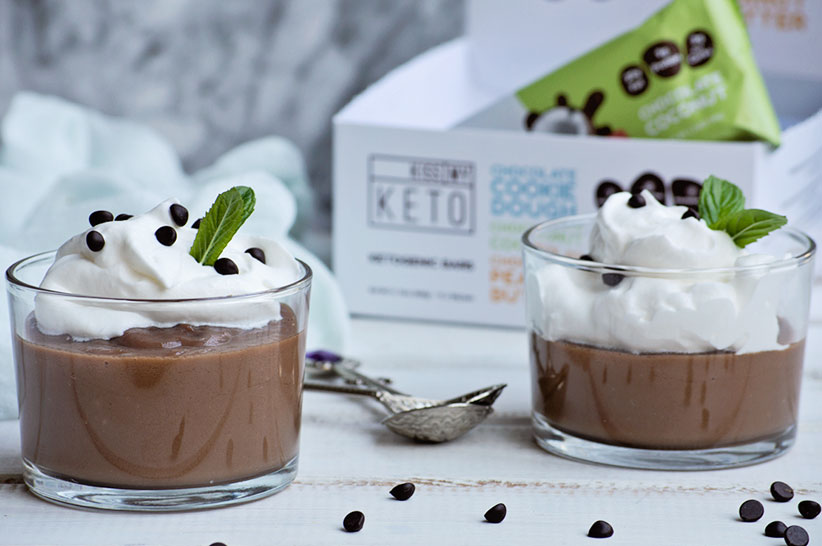 two cups of keto chocolate pudding with kmk bars in the background